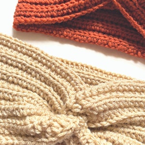 May include: Two crocheted headbands, one in a light beige color and one in a burnt orange color. Both headbands are twisted into a knot.