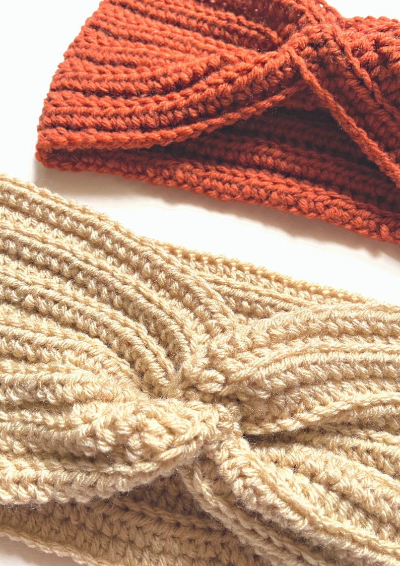 May include: Two crocheted headbands, one in a light beige color and one in a burnt orange color. Both headbands are twisted into a knot.