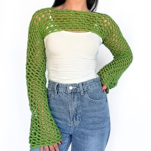 May include: A green crochet top with long sleeves and a wide neckline. The top is made of a lightweight, open-weave fabric.