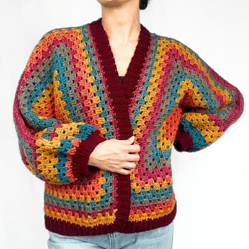 May include: A colorful crochet cardigan with a V-neck and long sleeves. The cardigan is made with a variety of colors, including red, orange, yellow, green, and blue. The cardigan is crocheted in a granny square pattern.