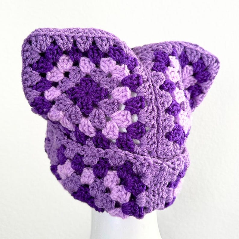 May include: A purple and lavender crocheted hat with a unique ear flap design.