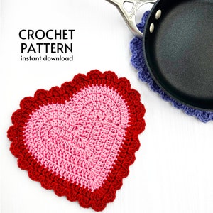 May include: A crochet heart-shaped hot pad in red and pink with a scalloped edge. The hot pad is on a white surface.
