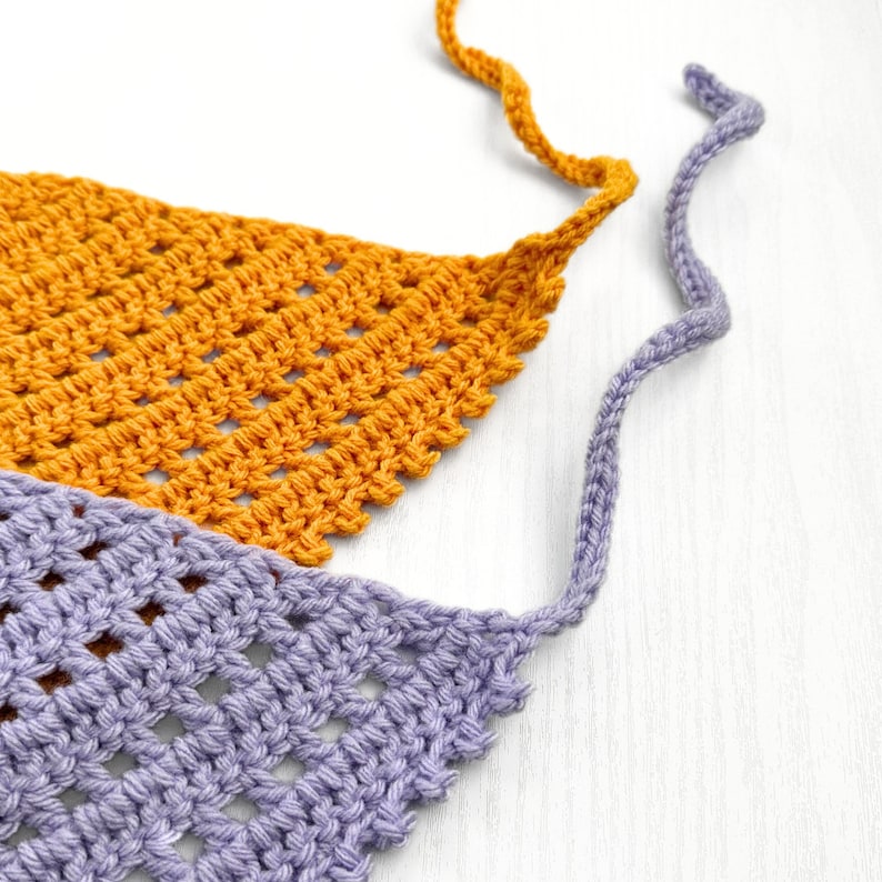 Puede incluir: Una bufanda triangular de ganchillo en color morado y naranja. La bufanda tiene flecos en los extremos y est&aacute; hecha con un patr&oacute;n de punto sencillo.