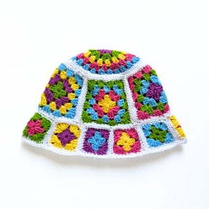 May include: A colorful crocheted bucket hat with a white brim and a pattern of squares in shades of green, pink, yellow, blue, and purple.
