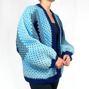 May include: A blue and navy crochet cardigan with a loose fit and long sleeves. The cardigan is made with a granny square stitch pattern.