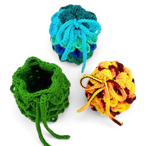 May include: Three small, round, crocheted drawstring pouches. One is solid green, one features a blue and teal scale-like pattern with a matching drawstring, and one displays a yellow, orange, and dark red variegated yarn pattern with a yellow drawstring.