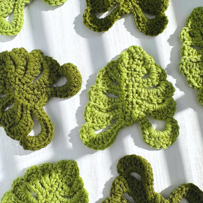 May include: A collection of crocheted green monstera leaves, a popular houseplant, on a white surface.