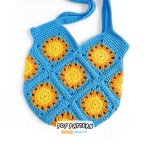 May include: A handmade crochet tote bag featuring a pattern of square motifs. Each square contains a bright yellow and orange sunburst design centered on a vibrant blue background. The bag includes a matching blue crochet strap for carrying.