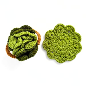 May include: Two crocheted green and orange coasters. One coaster is a round shape with a scalloped edge. The other coaster is a round ball shape.