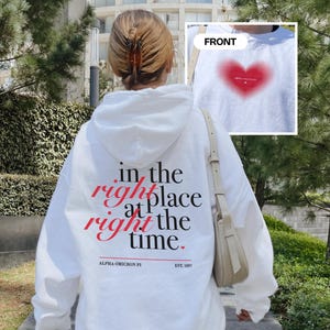 Back of a white sorority hoodie with the text “in the right place at the right time” in a serif font. The hoodie is customized for AOII and it's founding year. The front features a red blur heart design with the text Alpha Omicron Pi.
