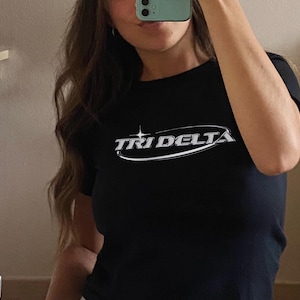 May include: Black t-shirt with a silver graphic that says "Tri Delta" in a curved font.