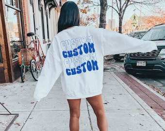 Pode incluir: Camisola branca com a palavra "CUSTOM" repetida quatro vezes em letras azuis em forma de bolha nas costas.