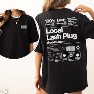 May include: Black oversized t-shirt with white text and a barcode on the front. The back of the shirt features the text "100% LASH SPECIALIST" and "Local Lash Plug @addcustom" with additional text and icons. The shirt is a casual style.