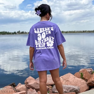 May include: Purple t-shirt with white text that says "Lauren's 30th Birthday Trip Miami Beach, Florida" with a white hibiscus flower graphic.