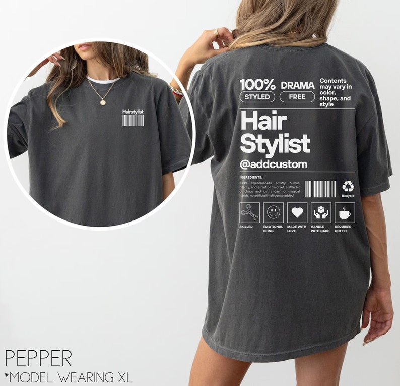 May include: A dark grey t-shirt with the text "Hair Stylist @addcustom" printed on the back. The shirt also features a graphic of a pair of scissors, a smiley face, a heart, a hand with care symbol, and a coffee cup.