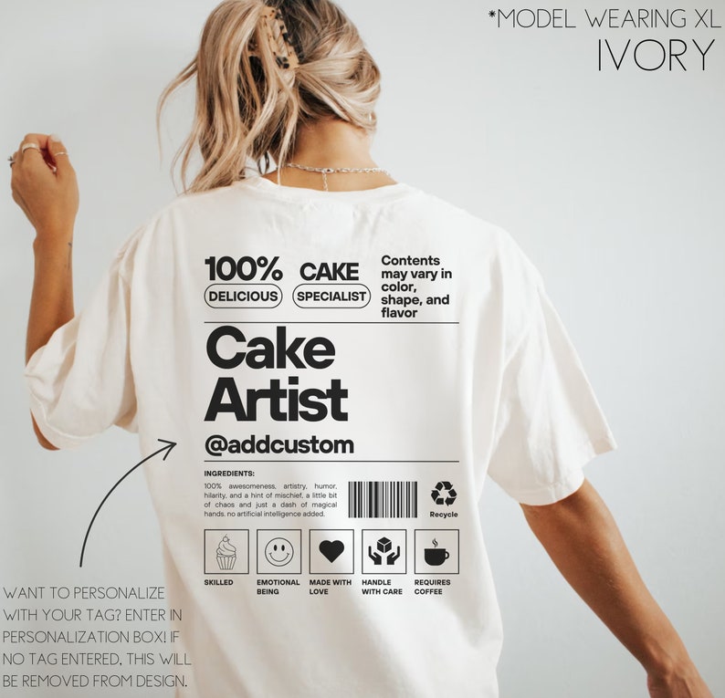 May include: White t-shirt with a black graphic design that says "100% Delicious Cake Specialist" and "Cake Artist @addcustom". The graphic also includes a barcode, a recycle symbol, and icons for skilled, emotional being, made with love, handle with care, and requires coffee.