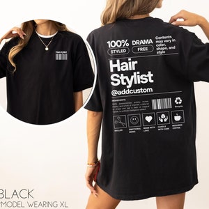 May include: Black t-shirt with a white graphic design that says "100% Drama Styled Free Hair Stylist @addcustom". The graphic design includes a barcode, a recycle symbol, and icons for skilled, emotional being, made with love, handle with care, and requires coffee.