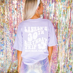 May include: A lavender t-shirt with white text that reads "Lauren's 30th Birthday Trip Miami Beach, Florida" with a white hibiscus flower graphic.