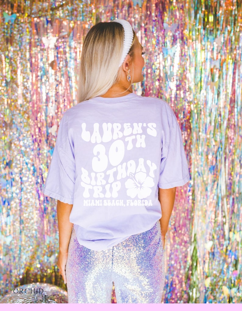 May include: A lavender t-shirt with white text that reads "Lauren's 30th Birthday Trip Miami Beach, Florida" with a white hibiscus flower graphic.