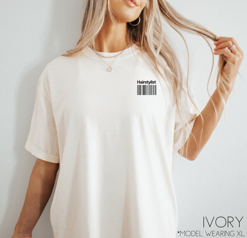 May include: Ivory t-shirt with the text "Hairstylist" and a barcode printed on the front. The model is wearing a size XL.