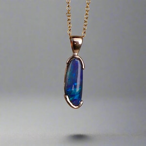 Può includere: Una collana con pendente dorato con un'opale a forma di goccia. L'opale mostra un vibrante gioco di colori, con sfumature di blu e verde. Il pendente è sospeso a una delicata catena d'oro, creando un gioiello elegante e accattivante.