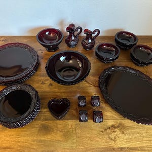 May include: A set of vintage red glass serving dishes, including a large oval platter, round serving bowls, and small dishes. The set features a decorative, raised pattern.
