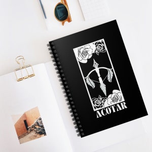 May include: A black spiral notebook with a white design featuring a bow and arrow with feathers and roses. The text "ACOTAR" is printed in white at the bottom of the design.