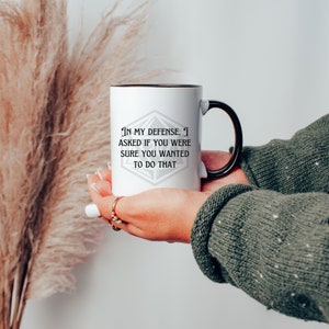 May include: White ceramic mug with a black rim and handle. The mug features a black and white graphic of a 20-sided die with the text "In my defense, I asked if you were sure you wanted to do that."