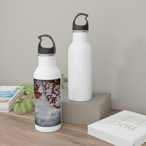 May include: Two stainless steel water bottles with black lids and carrying handles. One bottle has a colorful image of red leaves against a cloudy sky.