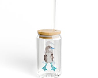 May include: A clear glass tumbler with a bamboo lid and a clear straw. The tumbler features a watercolor illustration of a blue-footed booby. The bird has brown and white feathers, blue feet, and a blue beak. The tumbler is designed for cold beverages.