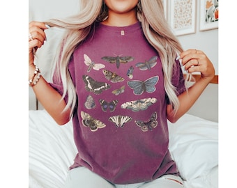 May include: A maroon t-shirt featuring a collection of illustrated butterflies in various sizes and colors. The butterflies are arranged across the front of the shirt, creating a nature-inspired design. The shirt has a relaxed fit.