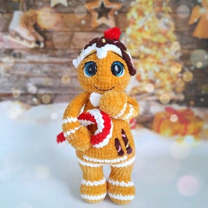 May include: A crocheted gingerbread person toy with white icing details, brown eyes, and a red and white candy cane. The toy is holding the candy cane in its hands.