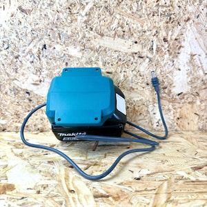 Peut inclure: Un chargeur de batterie Makita 5.0Ah de couleur bleu sarcelle et noir avec un cordon d'alimentation gris.