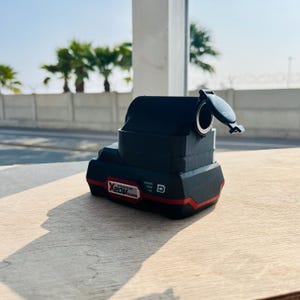 Puede incluir: Una batería de herramienta eléctrica negra y roja con una cubierta de plástico negro. La batería está etiquetada "X 20V MAX".