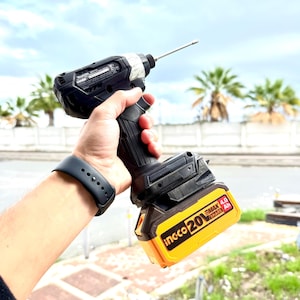 May include: Black and silver cordless impact driver with a yellow and black battery pack. The driver has a long silver bit extending from the front. The battery pack has the text "ingco 20V EMAX 4.0 Ah".