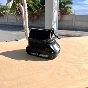 Può includere: Un caricabatterie Makita nero da 20Ah 18V con un coperchio in plastica nero.