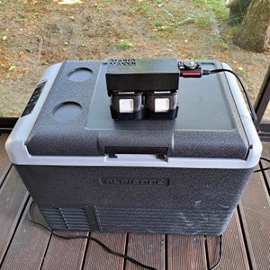 May include: A black portable refrigerator with a grey lid and a black power cord. The refrigerator has a black label that says "ALpicool" and a black box on top with the text "MARIA MAKER".