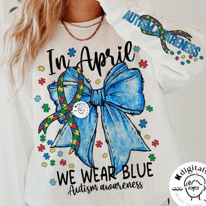 May include: White long-sleeve shirt with a blue ribbon bow and puzzle pieces. The shirt has the text "In April We Wear Blue Autism Awareness" printed on it.