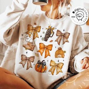 May include: Cream-colored sweatshirt featuring a collection of fall-themed illustrations. The design includes bows, a pumpkin, a leopard-print mug, and a beanie. The words "digital download" are at the bottom of the image.
