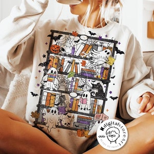 May include: Cream-colored sweatshirt featuring a Halloween-themed bookshelf design. The graphic includes books, ghosts, pumpkins, bats, and spiderwebs. The words "digital download" are printed at the bottom of the image.