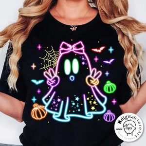 May include: Black t-shirt featuring a neon ghost design with peace signs, pumpkins, bats, and stars. The ghost has a bow and is surrounded by a neon outline. The words "digital download" are at the bottom.