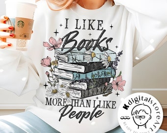 Op de afbeelding: Wit sweatshirt met een grafisch ontwerp van een stapel boeken met bloemen en de tekst "Ik hou meer van boeken dan van mensen".