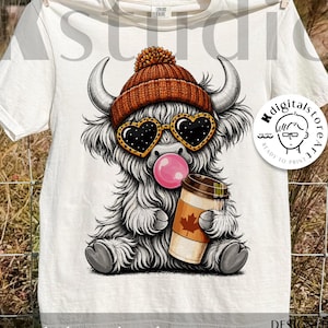 May include: White t-shirt featuring a cartoon Highland cow wearing a brown knit hat, heart-shaped sunglasses, and blowing a bubble. The cow is holding a coffee cup with a maple leaf design. Text on the shirt reads "digital download".