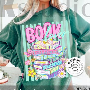 May include: Green sweatshirt featuring the text "BOOK Lover" in pink and blue, with a stack of colourful books and floral details. The design also includes the text "digital download" and "DESIGNED BY Kstudio".