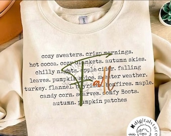 May include: A cream-colored sweatshirt with the word "Fall" in green and orange script. The sweatshirt features a list of autumn-themed words such as "cozy sweaters," "pumpkin spice," and "bonfires."