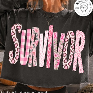 Op de afbeelding: Een antracietgrijze cropped sweater met het woord SURVIVOR in grote, gestileerde letters. Elke letter heeft een ander patroon, waaronder roze luipaardprint, roze gingham, roze bloemmotieven en roze lintjes voor borstkankerbewustzijn.