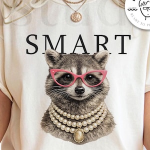 May include: Cream-colored t-shirt with the word "SMART" in black. The shirt features a raccoon wearing pink glasses and a pearl necklace. The words "digital download" are at the bottom of the image.