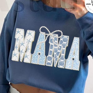 Puede incluir: Una sudadera azul marino con la palabra "MAMA" en blanco y azul claro, decorada con estrellas de mar, conchas y perlas. También se ven las palabras "digital download" y "designed by Kstudio".
