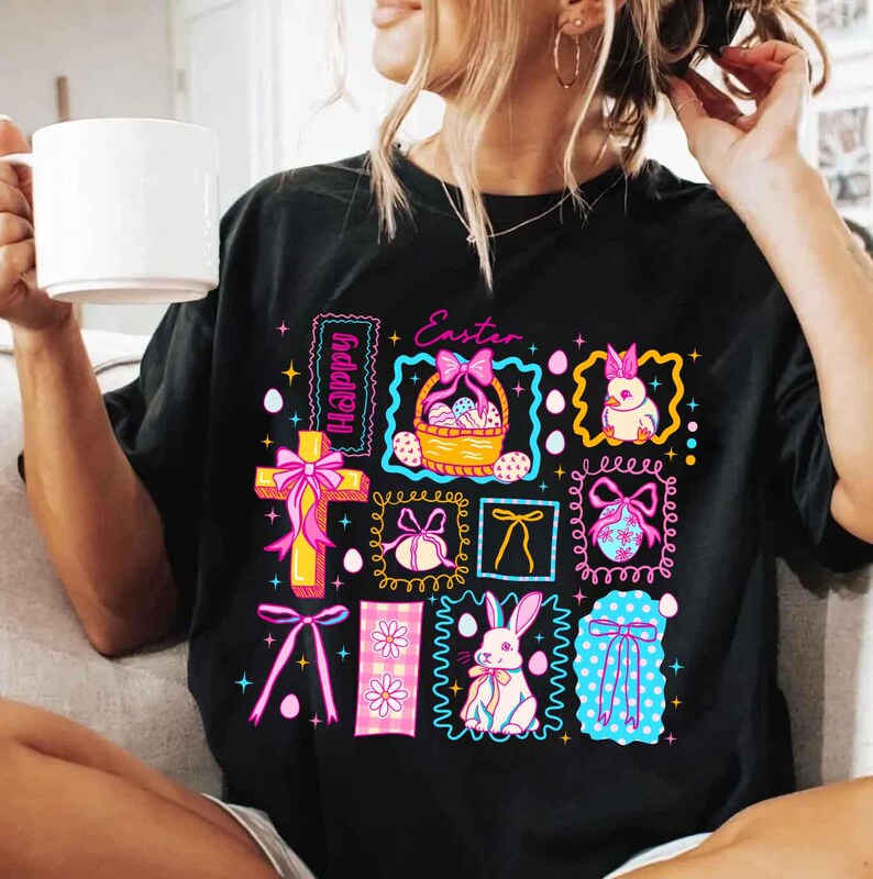 May include: Black t-shirt with a colorful Easter-themed graphic. The design includes a cross, Easter eggs, bunnies, and bows, with the word "Happy" and "Easter" in the design. The graphic is framed with decorative borders.