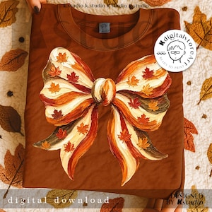 Op de afbeelding: Een bruine sweatshirt met een groot strikdesign versierd met herfstbladeren. De strik heeft crème, oranje en bruine strepen, met rode en gele esdoornbladeren. De woorden "digital download" staan onderaan.